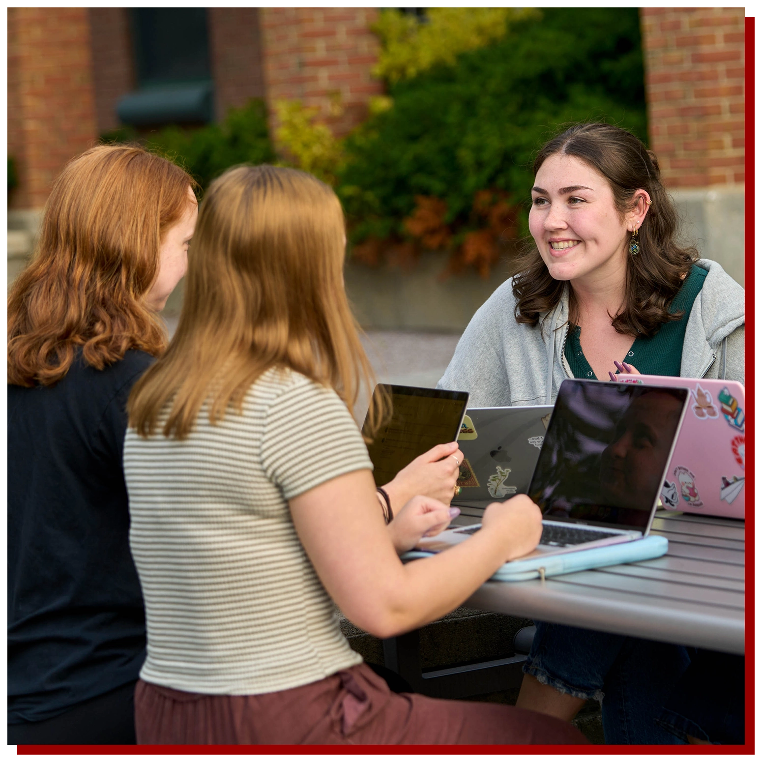 SUNY Stony Brook University College of Business Peer Mentoring Session Outside with 3 Students Talking at a Table with laptops on the table