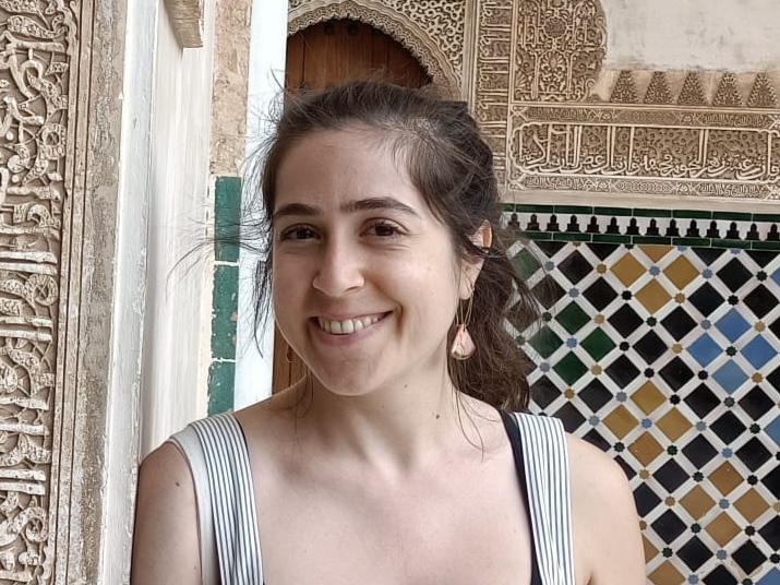 Person smiling, standing in front of ornate tile work and carved wooden door 