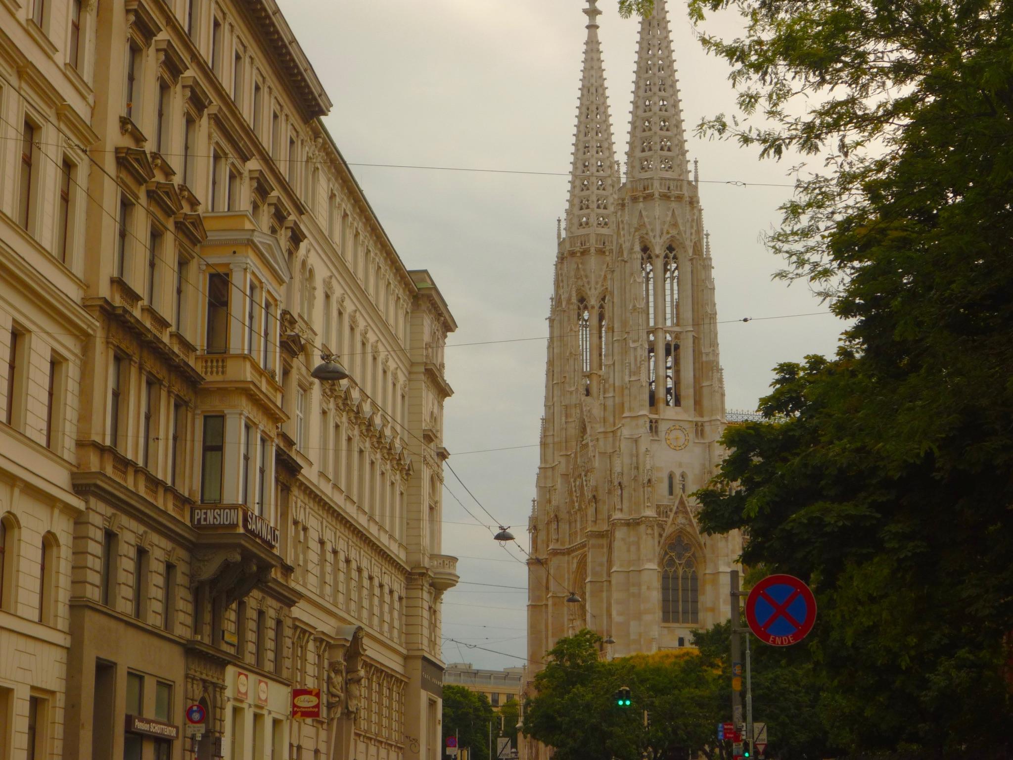 View of Votive Church's spire between classic European architecture on a cloudy day in Vienna.