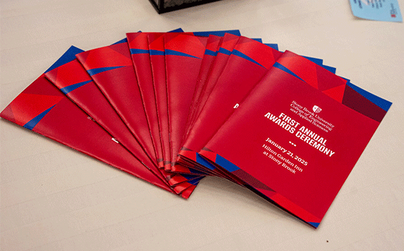 CEAS Award Program A stack of red and blue event programs for the First Annual Awards Ceremony, held on January 23, 2025, at Stony Brook University, displayed on a table.